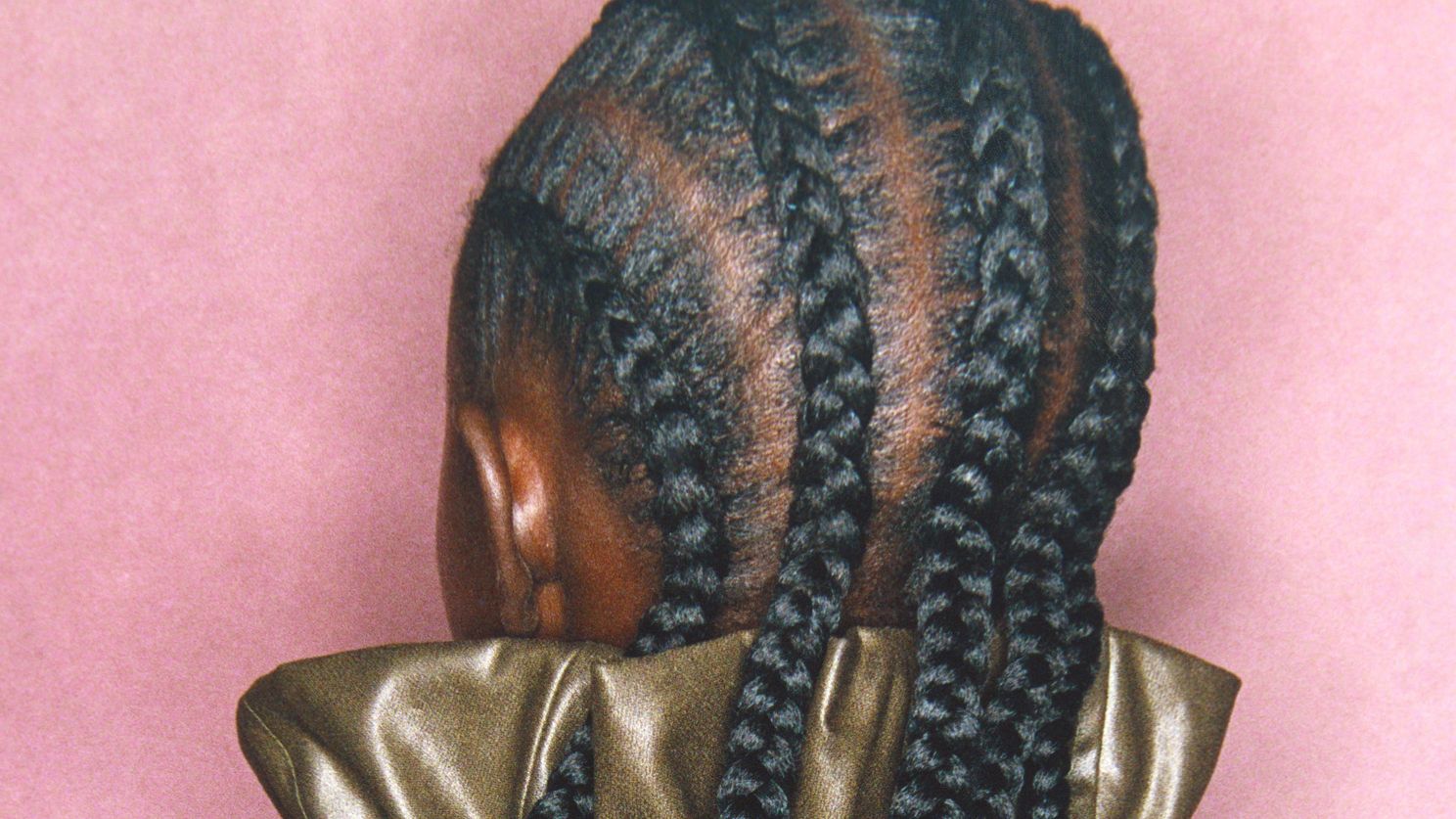 Model with cornrow braids facing away from the camera towards a pink wall
