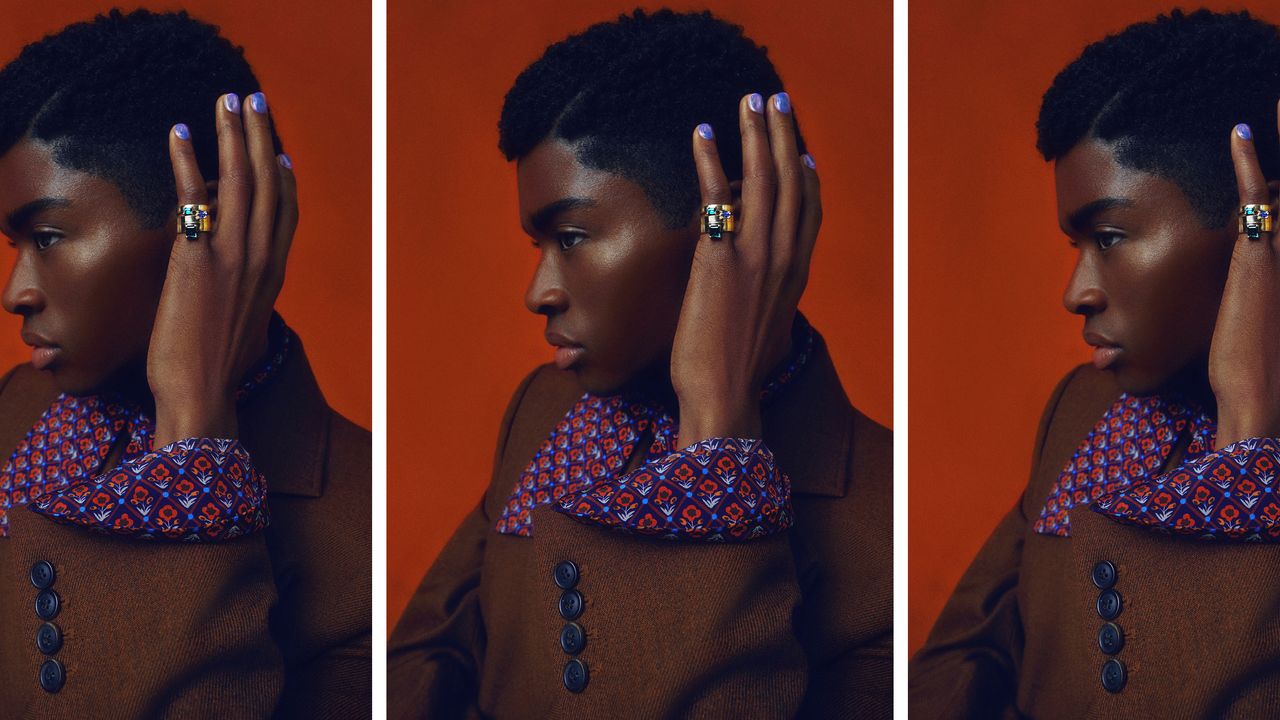 model with brown suit patterned shirt and blue manicure showing off their nails