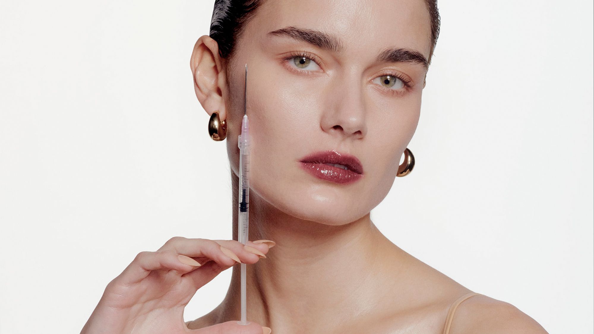 A woman holds a syringe near her cheek.