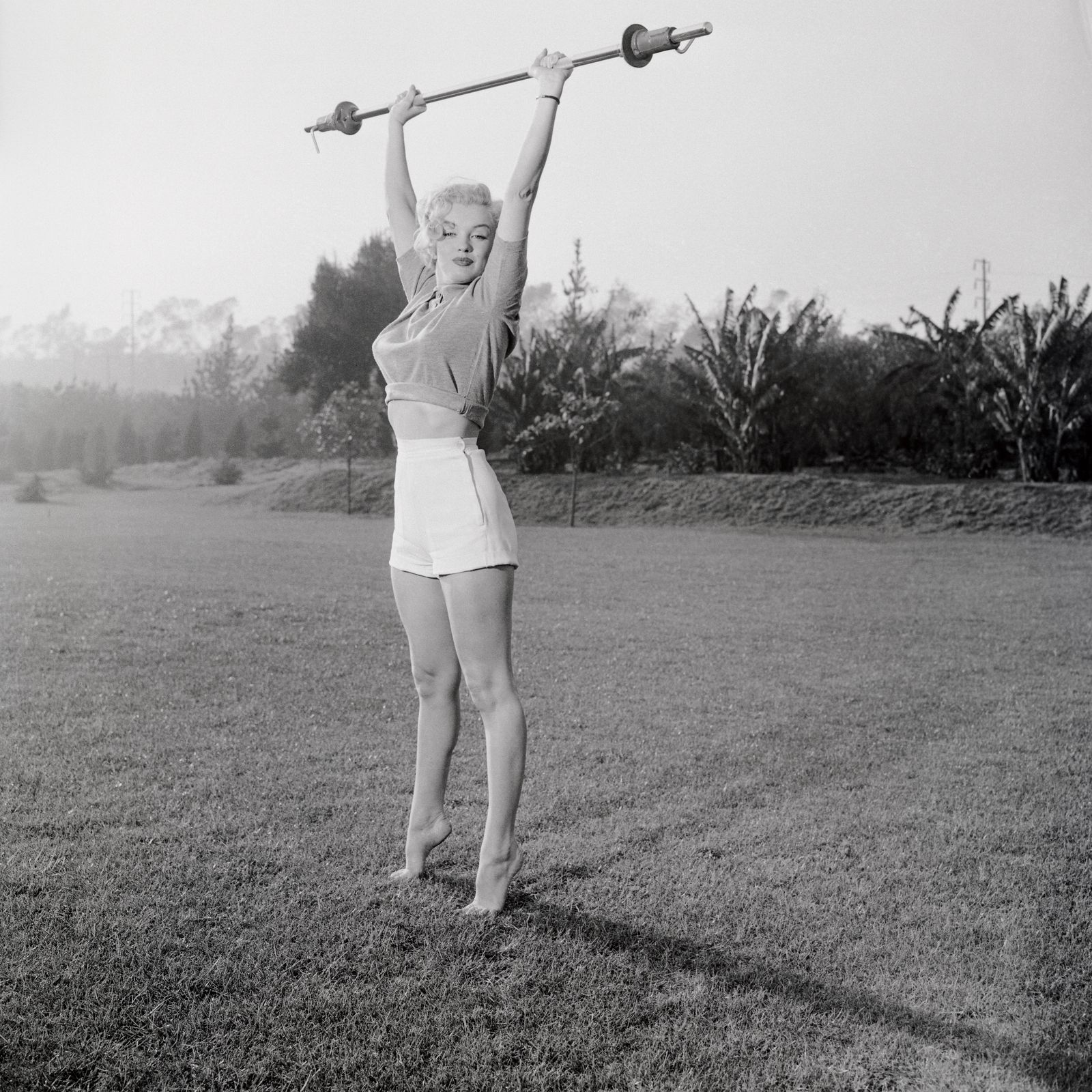 Marilyn Monroe reaching for the sky on tiptoe holding a light barbell.