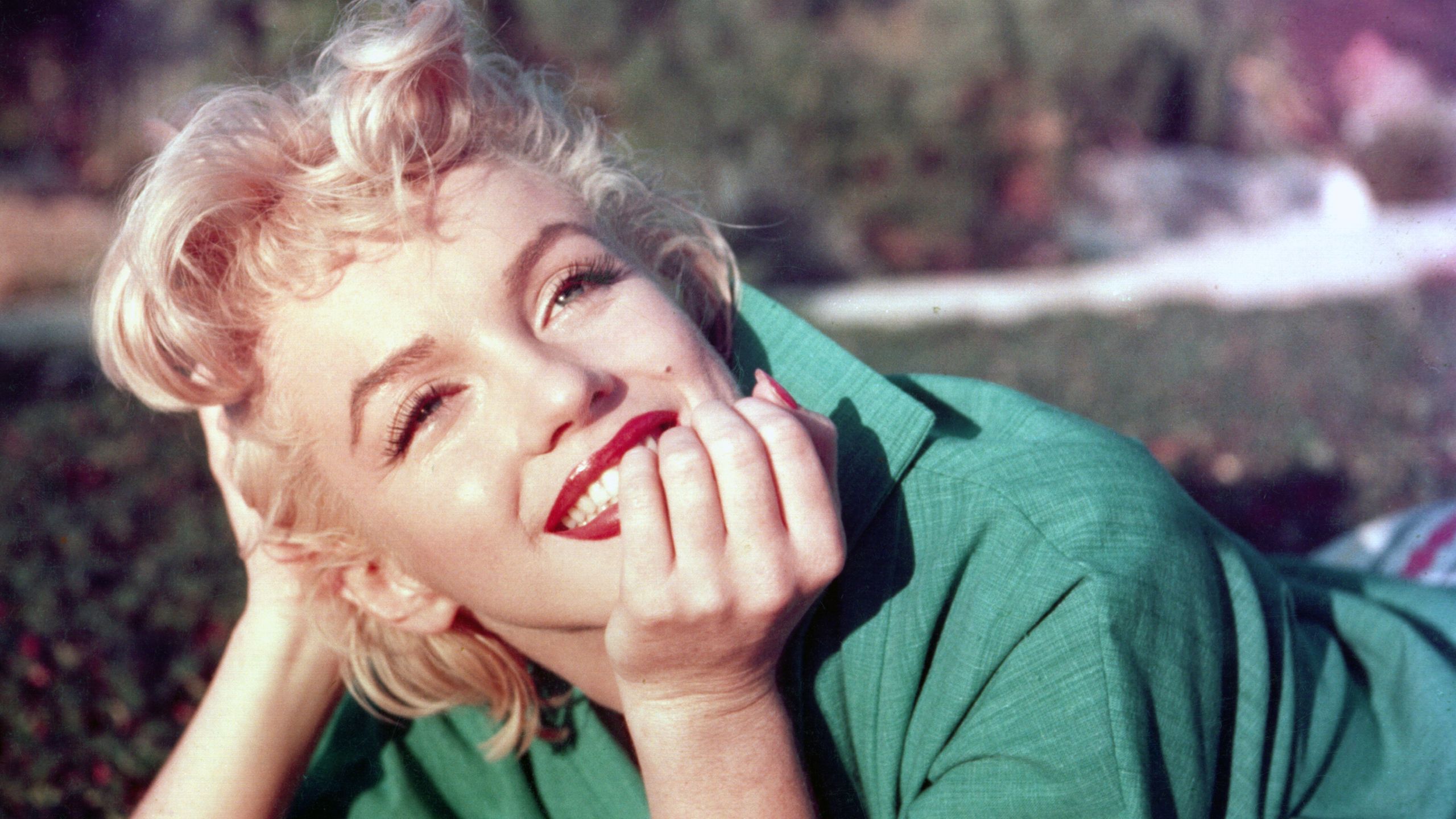 Marilyn Monroe poses in the grass in a green shirt.