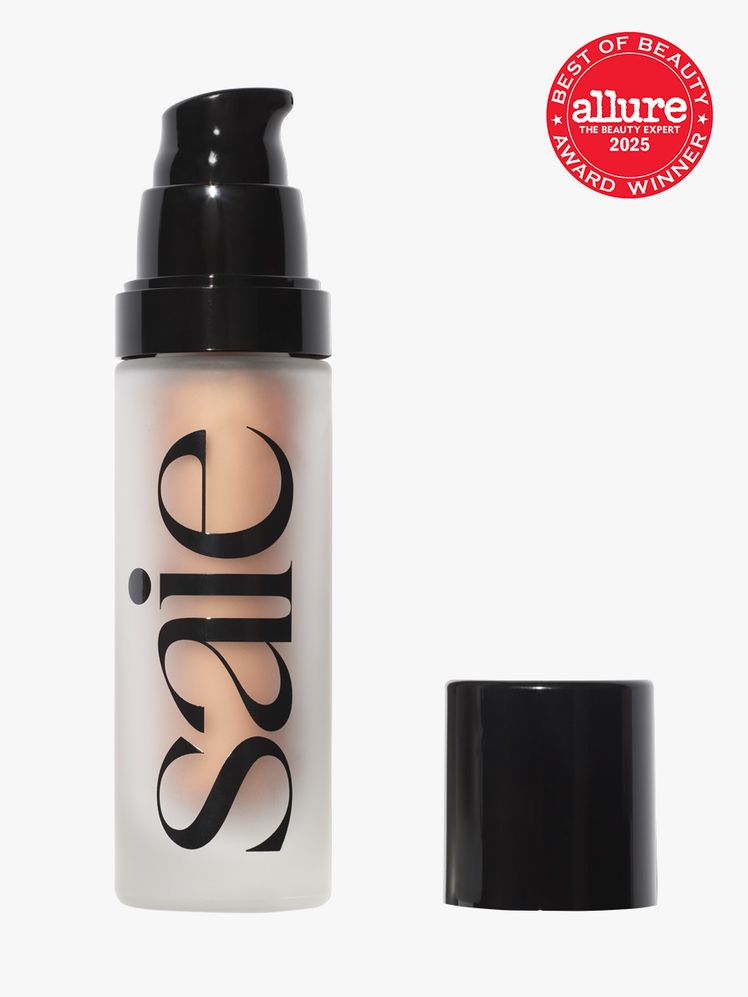 Saie Glowy Super Gel cloudy bottle of champagne gel primer with black pump and cap on light gray background with red...