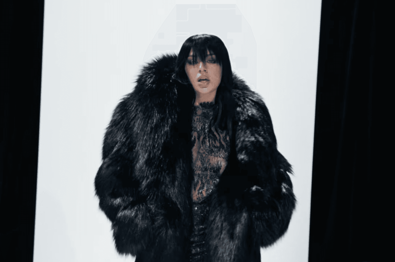 Charli XCX walks the runway in a black fauxfur coat lace top and long hair styled with bangs.